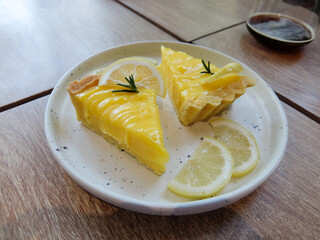 Lemon Tart is served on a white tiled plate decorated with thin slices of lemon.