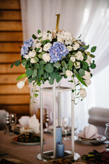 A composition of flowers and green, candle is on a festive table at the wedding banquet hall. Close up.