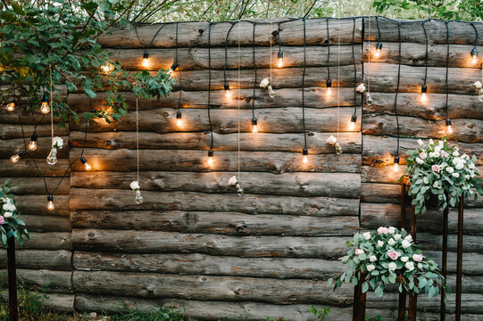 Wooden wall decorated garland with luminous bulbs and electric lamps decorated flowers. Original wedding floral decoration.  Wedding. Reception. Lounge zone.