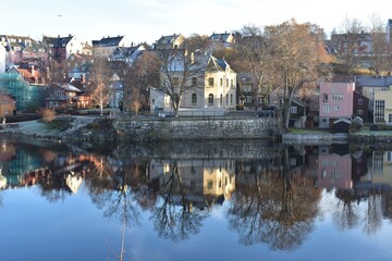 Cityscape of Trondheim city  and leafless tree reflection in the water at  Nidelva river Norway in early winter. 