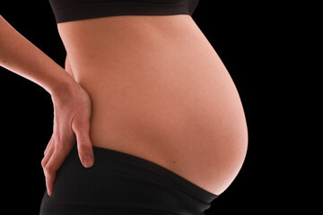 close up view of pregnant belly. Woman in black underwear isolated on black background.