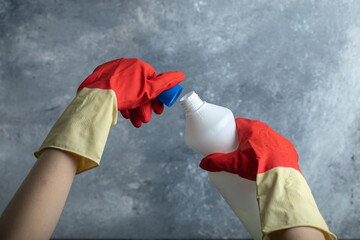 Hands in red gloves opening container of bleach