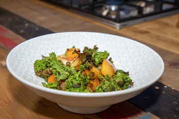 A delicious plate of Roasts Roots with Apple Kale and Crispy Seeds on a wooden kitchen work top