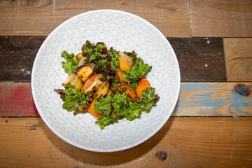 A delicious plate of Roasts Roots with Apple Kale and Crispy Seeds on a wooden kitchen work top