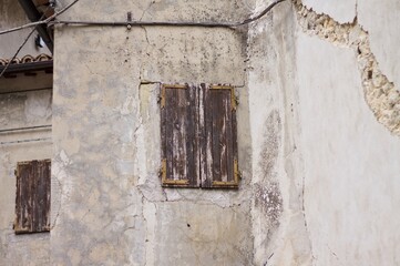 A closed window with wooden shutters in an abandoned building with cracks due to the earthquake (Marche, Italy, Europe)