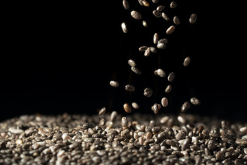 Close up of chia seeds falling and landing in to a large pile with background fading to black