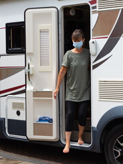 A lady motor homer steps out of the side door of her recreational vehicle wearing a face mask.She has bare feet.Summer