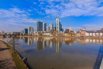 Fototapeta na wymiar Financial district with skyscraper of Frankfurt am Main. River with reflections in the foreground on a sunny day. Bank on the river in spring