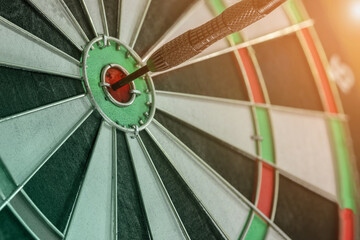 Close up shot arrow hit in the target center of dartboard on light on of dartboard to represent that the business reached the target of company on retro filter tone picture style. target and goal