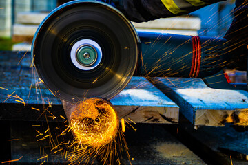 Close-up on the sides fly bright sparks from the angle grinder machine. A young male grinds a metal pipe with an angle grinder on a construction area