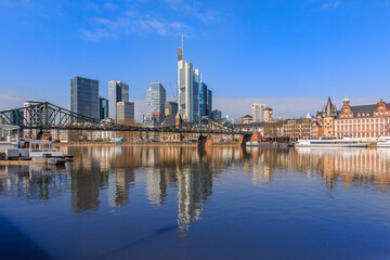Frankfurt skyline in sunshine. Commercial buildings and bridge over the river Main with reflections. Ships at the moorings and historic buildings