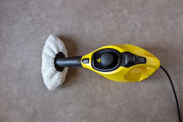 Obraz premium Yellow steam cleaner with a washcloth on a brown background, top view