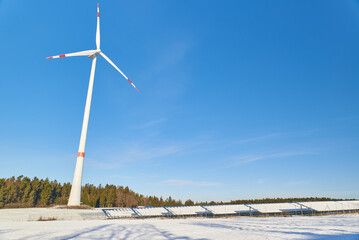Low angle shot of a wind power plant and a snow covered photovolatic system.
