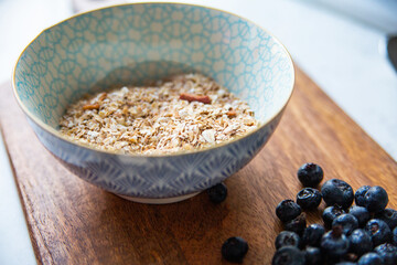 Granola, muesli, oatmeal in a bowl and blueberry on a wooden cutting board.