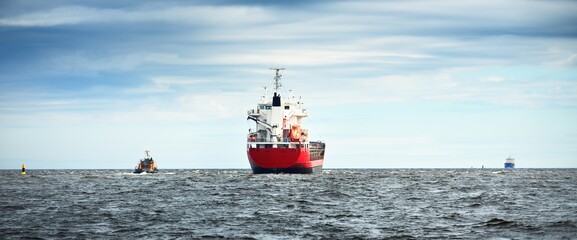 General cargo ship next to a tugboat in an open Baltic sea. Klaipeda, Lithuania. Nautical vessel, freight transportation, global communications, industry, commerce. Dramatic cloudscape © Alex Stemmer