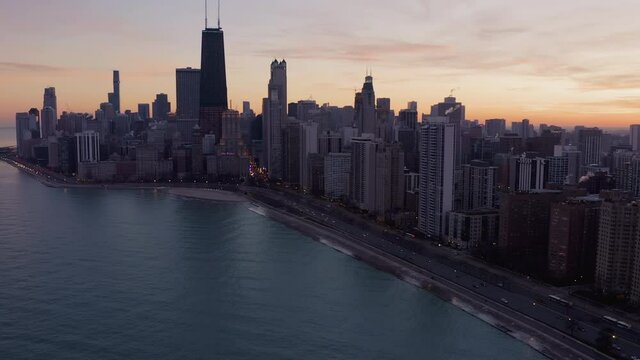 Flying above Chicago downtown and Lake Michigan at dusk. Busy road by the beach and city lights