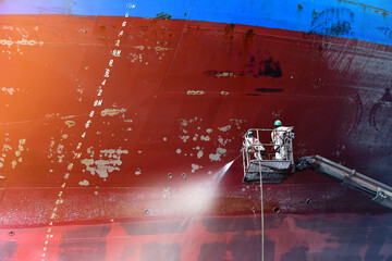 Worker cleaning and washing with Cargo ship on sherry picker car by high pressure water gun cleaning under repair in floating dry dock in  shipyard Thailand