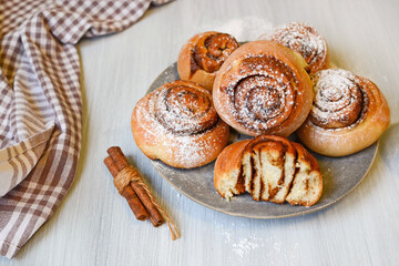 fresh homemade yeast dough buns with cinnamon and powdered sugar on white wooden background