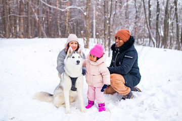 Fototapeta na wymiar afro man with his caucasian wife having fun with a beautiful daughter playing husky in snowy park