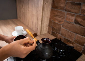 A young woman adds a spoonful of ground coffee to a coffee cup. View of the hands with a spoon.