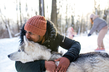 mixed race man hug his dog husky in winter forest park
