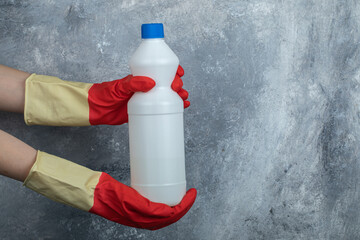 Hands in red gloves holding container of bleach - obrazy, fototapety, plakaty
