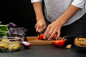 Cooking process, woman cutting tomatoes for aubergine paste from stocked eggplants