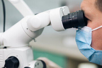 Dentist using dental microscope and examining woman's teeth. Medium shot of male dentist in scrubs and face mask using dental microscope while examining patient