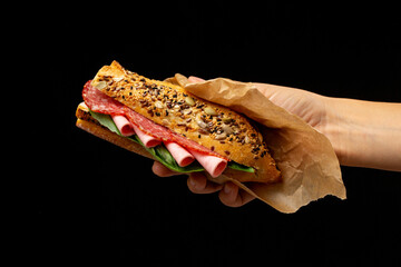 Tasty sandwich in baguette with ham and salami in hand