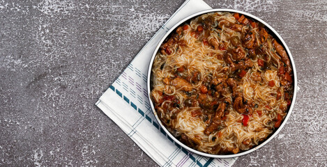 Rice noodles with meat and vegetables on a round plate on a dark background. Top view, flat lay