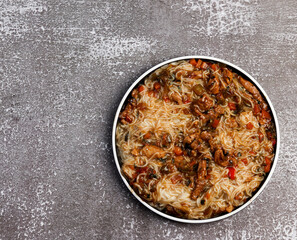 Rice noodles with meat and vegetables on a round plate on a dark background. Top view, flat lay