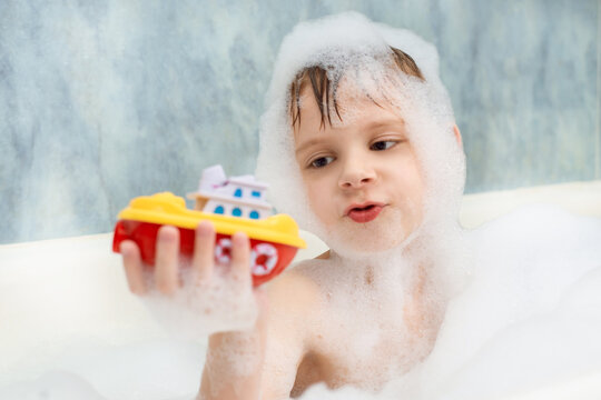 The boy plays with a boat in a bath in soapy water. Hygiene, cleanliness concept. Children's games in the bathroom.