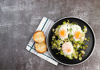 Fried eggs with leek on a round plate on a dark background. Top view, flat lay