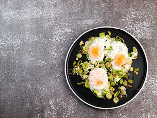 Fried eggs with leek on a round plate on a dark background. Top view, flat lay