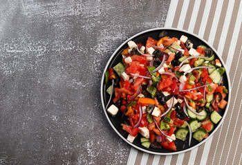 Greek salad with olives, tomatoes, cucumbers, pink onions and feta cheese on a round plate on a dark background. Top view, flat lay.