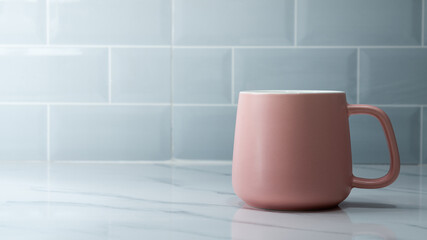 A pastel pink coffee cup or mug glass is placed on marble floor with space of brick tile as background. Photo applied extra exposure as sunlight and high contrast ration. Selective focus.
