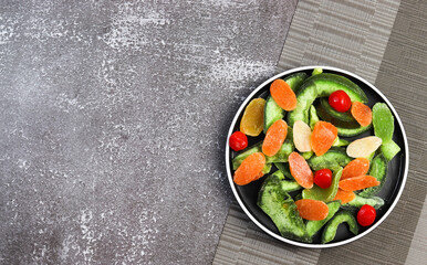 Candied pomelo, pineapple, kumquat on a round plate on a dark background. Top view, flat lay