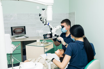 Dentist in latex gloves examining patient teeth in clinic. Patient lying with his open mouth in dentists office. Stomatologist performing examination using a microscope