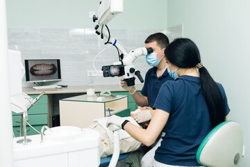 Medical Stomatology Concept. Doctor making teeth examination research survey using microscope in dentistry. Dentist is treating patient in modern dental office