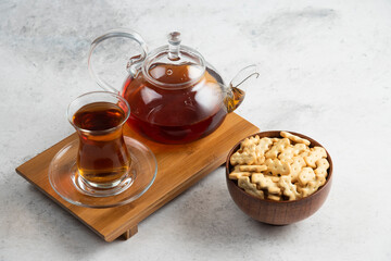A glass cup of tea with wooden bowl full of crackers