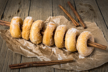 Sugared mini donuts lined up on a cinnamon stick on a wooden table