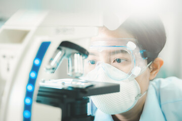 Doctor or scientist looking through a microscope in medical research lab or science laboratory.