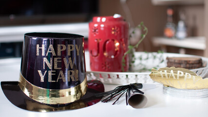 Black top hat and golden crown with happy new year wishes written on it on a white table in a living room