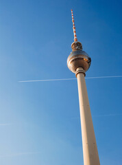 Berlin TV tower against a blue sky with a trail from the plane.