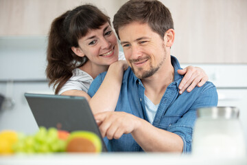 cheerful young couple cooking with recipe on a tablet