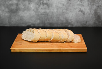 Baguette cut in slices on wooden breadboard over a black stone background. Rustic bread concept