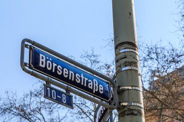 blue street sign stock exchange on a gray lamppost with fixings. House number eight to ten on sign. House with window facade and trees in spring in the background