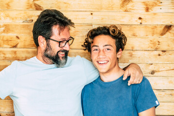 Father and son portrait - adult and young teenager generations smile and hug together with wooden...