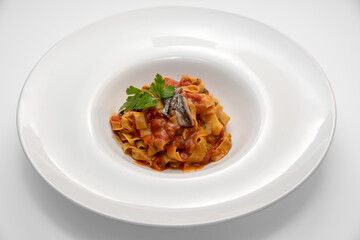 Tagliatelle with red tomato sauce, anchovy and parsley leaves, typical Italian egg pasta in white dish on white background