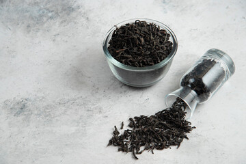 Dry tea leaves in a glass bowl on a marble background
